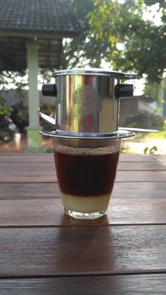 a coffee cup sitting on top of a wooden table next to a metal pot filled with liquid