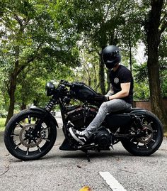 a man sitting on top of a motorcycle in the middle of a parking lot next to trees