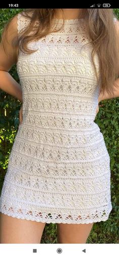 a woman wearing a white crochet dress with her hands on her hips, posing for the camera