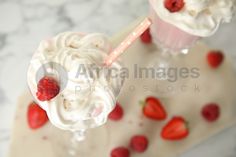 two glasses filled with whipped cream and strawberries on top of a marble table next to each other