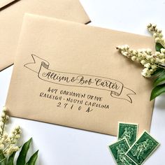 two envelopes with stamps on them sitting next to each other and flowers in the background