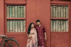 a man and woman standing next to each other in front of a red building with windows