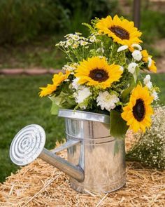 a metal watering can filled with sunflowers and white daisies on top of straw