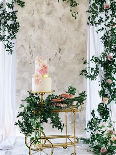 a table topped with a cake next to a wall covered in vines and pink flowers