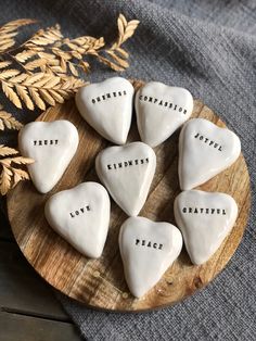 white ceramic hearts with words written on them sitting on a wooden plate next to some plants