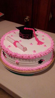 a graduation cake with pink frosting and decorations