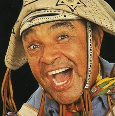 an old man wearing a hat with his mouth wide open and smiling at the camera