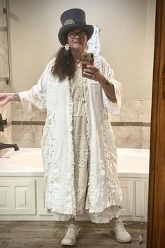 a woman in a white dress and hat taking a selfie with her cell phone