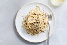 a white plate topped with pasta next to a glass of wine