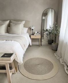 a bedroom with a round rug on the floor next to a white bed and mirror