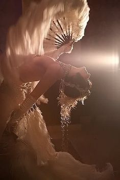 a woman dressed in white with feathers on her head and hands holding an umbrella over her head