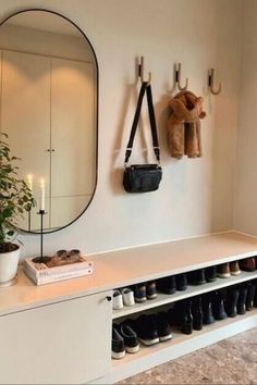 a white bench with shoes on it next to a wall mounted mirror and coat rack