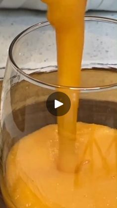 an orange juice being poured into a glass with a yellow liquid in the bottom and inside