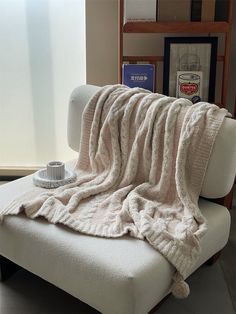 a white couch covered in a blanket next to a book shelf with books on it