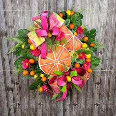 an overhead view of a wreath with oranges, pink flowers and green leaves on a wooden fence