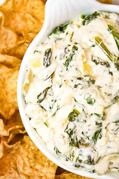 a white bowl filled with spinach dip surrounded by tortilla chips