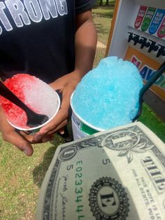 a man holding two buckets filled with blue and red jello next to a dollar bill