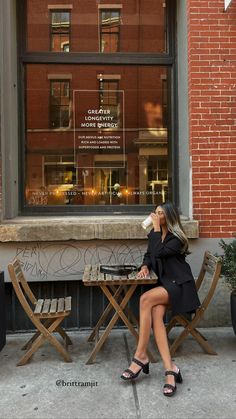 a woman sitting at a table drinking from a cup in front of a store window