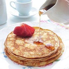 pancakes on a plate with syrup being drizzled over them and topped with strawberries