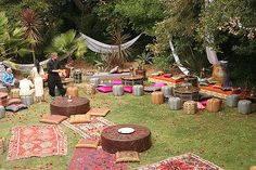 a group of people sitting on top of a lush green field covered in lots of rugs