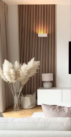 a white bed sitting in a bedroom next to a tall vase with some flowers on it