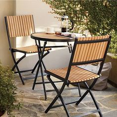 two folding chairs and a table on a stone patio with plants in the back ground