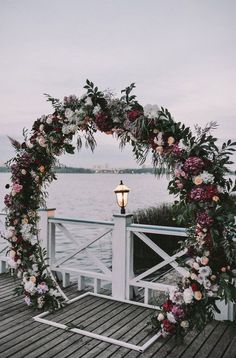 a wedding arch decorated with flowers and greenery on a pier by the water at dusk