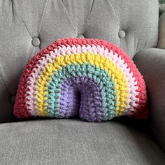 a crocheted rainbow pillow sitting on top of a gray couch next to a grey chair