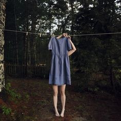 a woman in a blue dress is hanging on a clothes line with trees behind her