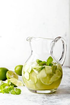 a pitcher filled with ice and limes on top of a table next to sliced limes