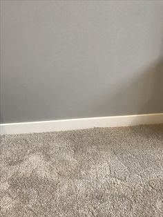 the corner of a room with carpeting and a wall painted in light gray color