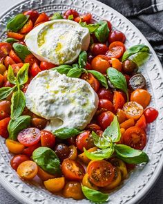 a white plate topped with tomatoes, cheese and spinach on top of a table