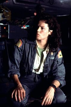 a woman in uniform sitting on the ground with her hands crossed and looking off to the side