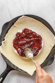 someone is spooning sauce into a skillet with dough on the side and another hand holding a spoon