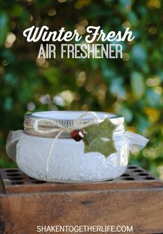 a glass jar filled with air freshener sitting on top of a wooden box next to trees