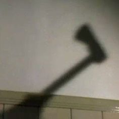 the shadow of an old hammer is shown in front of a white wall with tiles