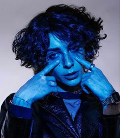 a man with blue paint on his face is holding his hands to his ears and looking at the camera