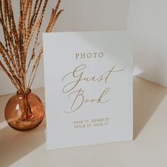 a photo guest book next to a vase with dried grass in it on a table