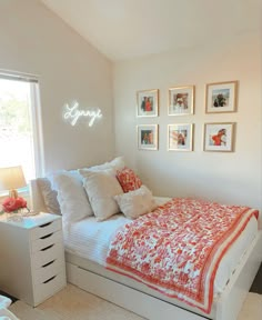 a bedroom with white walls and pictures on the wall above the bed, along with an orange and white bedspread