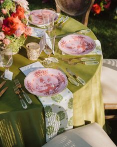 the table is set with pink and green plates, silverware, and flowers in vases