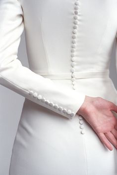 a woman wearing a white dress with pearls on the sleeves and arms, holding her hands together