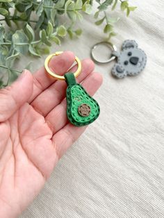 a hand holding a green crocheted keychain and two other items in the background