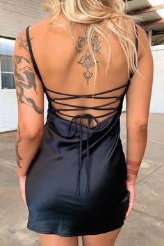 the back of a woman wearing a black dress with tattoos on her arms and legs