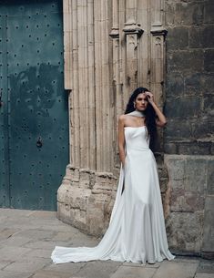 a woman standing in front of a building wearing a white dress and holding her hand on her head