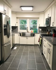 a kitchen with black and white tile flooring, stainless steel appliances and sink area