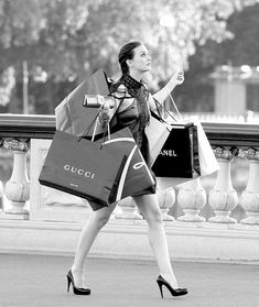 black and white photograph of a woman carrying shopping bags while walking down the street with her hand up in the air