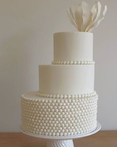 a three tiered white cake with pearls and a flower on top