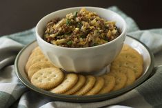 a white bowl filled with food sitting on top of a plate next to crackers