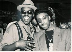 two men standing next to each other in front of a crowd wearing sunglasses and hats