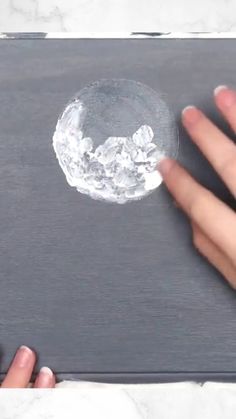 two hands are holding a piece of ice on top of a gray surface with white marble